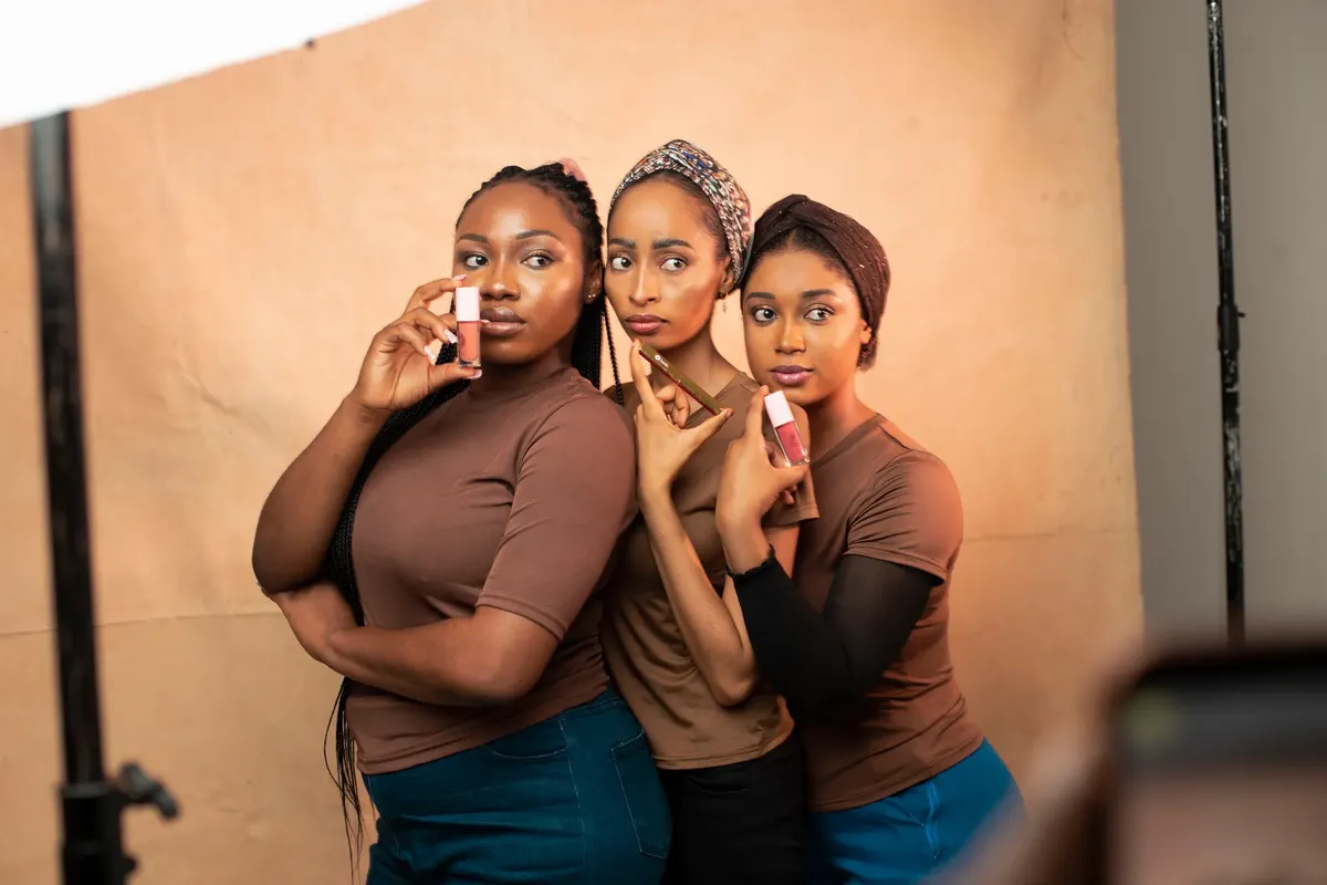 Three women showcasing makeup products in a professional studio environment.