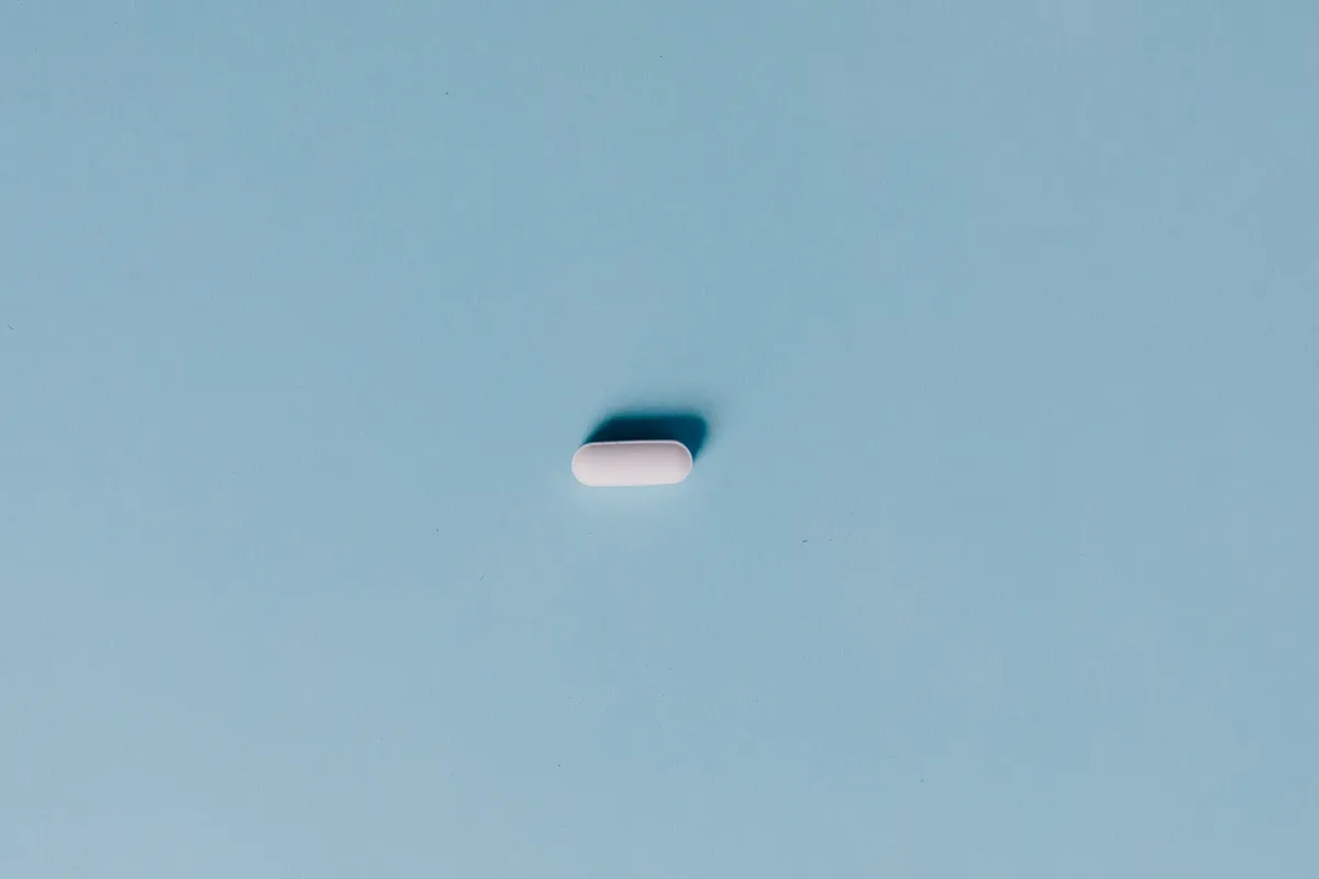 Single white pill on a blue background, representing medicine or healthcare.