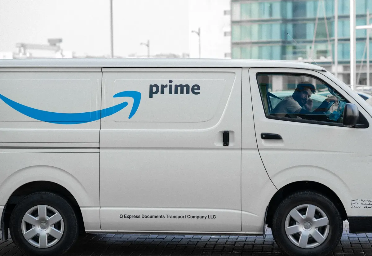 一輛白色配送車載有Prime標誌停在都市街道上，車內有駕駛員。