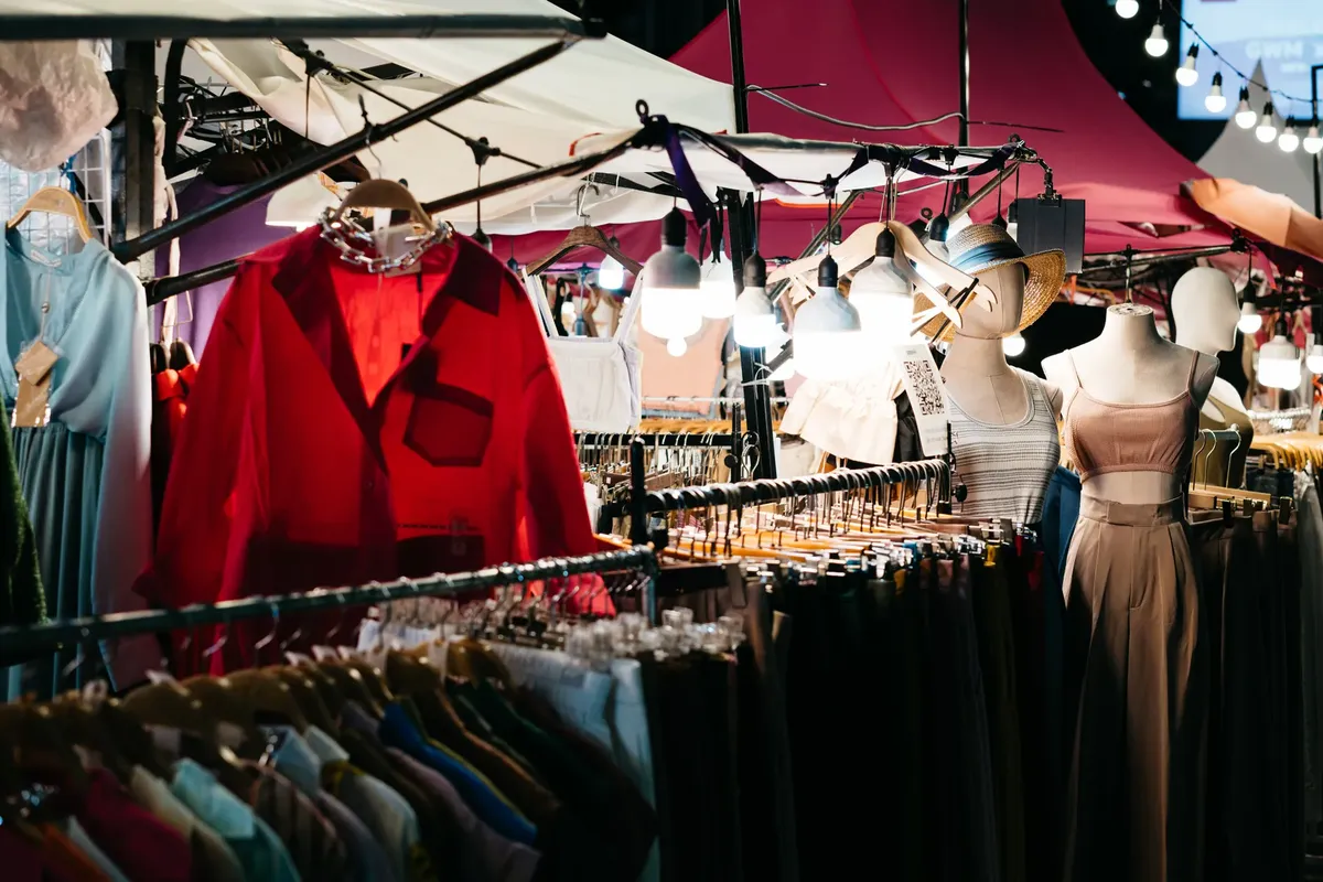 Colorful illuminated clothing stalls at a bustling outdoor night market.