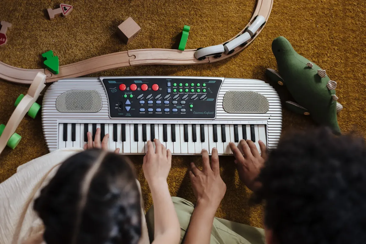子どもが床に玩具の電車とぬいぐるみの恐竜を抱きしめている様子の上からの眺め。