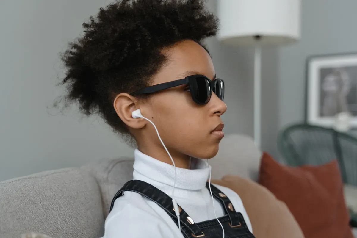 Profile of a young child with sunglasses and earphones indoors, showcasing self-expression.