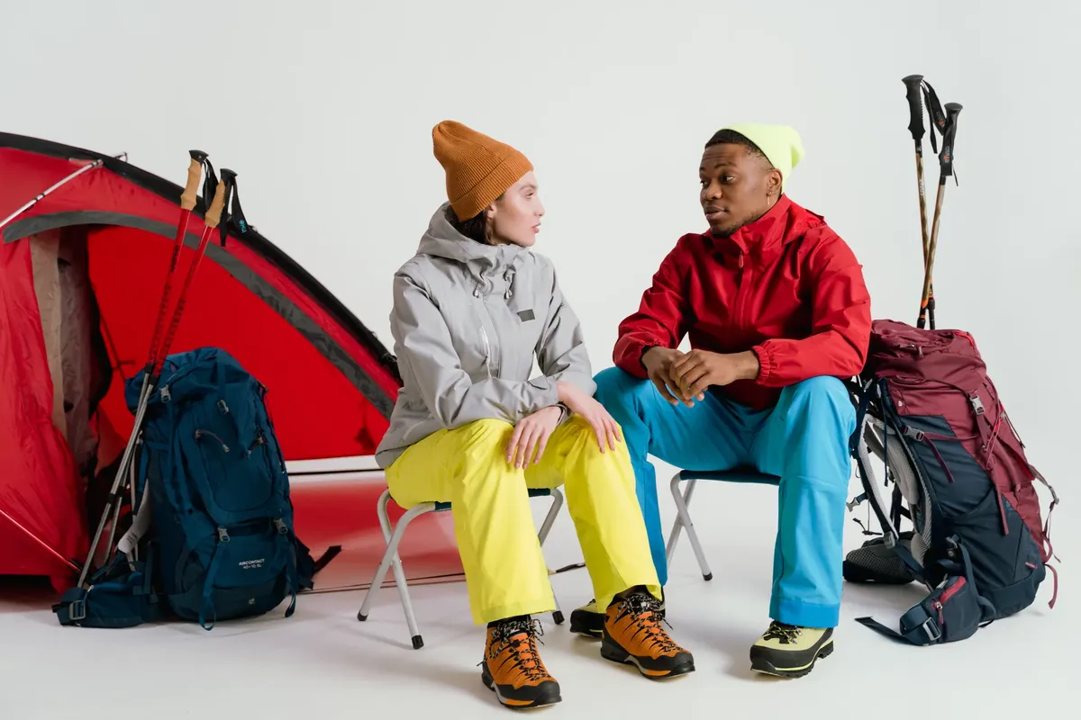 Two campers sit with hiking gear and tent in a studio setting.